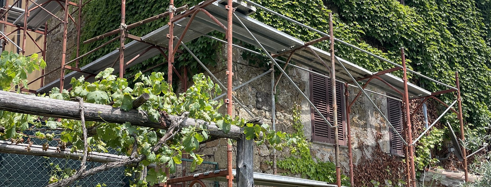 An ivy-covered stone house under restoration, with a vine pergola
