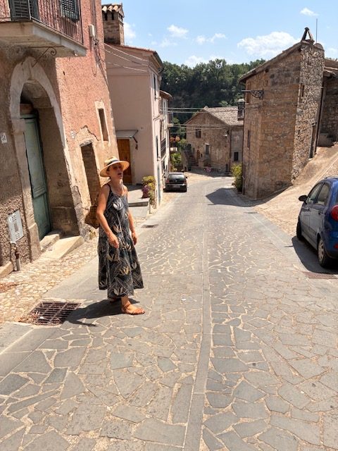 A woman in a straw hat walking a village street, seen from behind